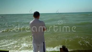 一个年轻人站在海滩上看着海浪。 海浪拍打着海岸. 慢动作。